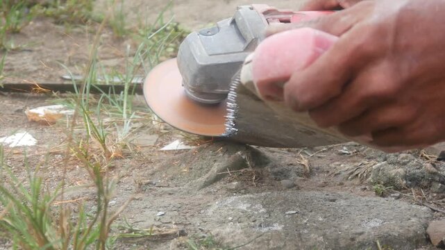Workers are sharpening or cutting saw blades using a hand grinder in an open area.
