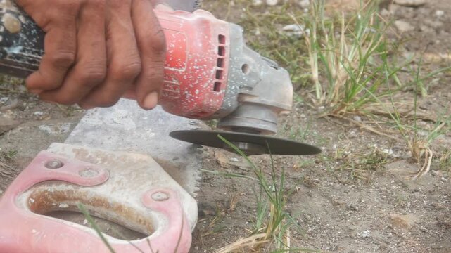 Workers are sharpening or cutting saw blades using a hand grinder in an open area.