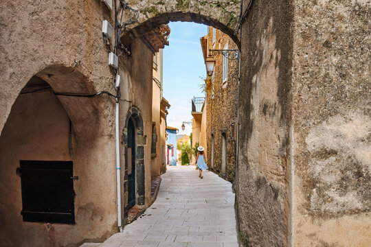 A young woman walks along a narrow alley past a stone archway in the medieval old town center of the hill town of Gassin, France, a commune in the Var department, Provence-Alpes-C&ocirc;te d'Azur region.