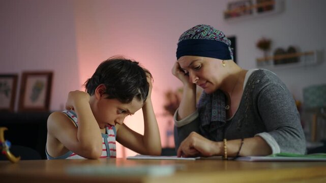 Mother supporting son with homework at table in evening, patient parenting and learning guidance in home education routine, focus and encouragement in family study moment