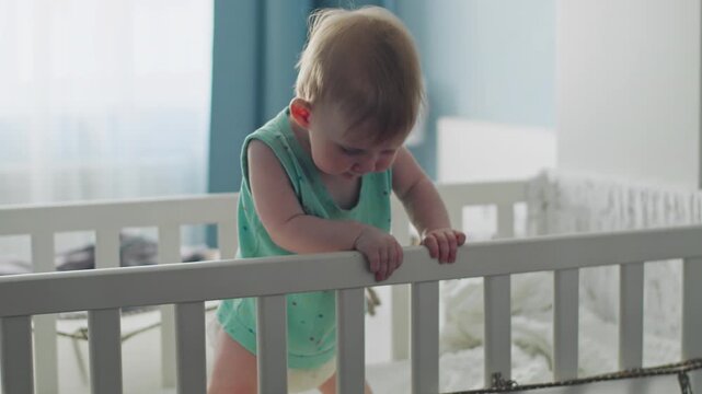 Baby girl standing in crib with support, practicing balance. Baby milestones early independence