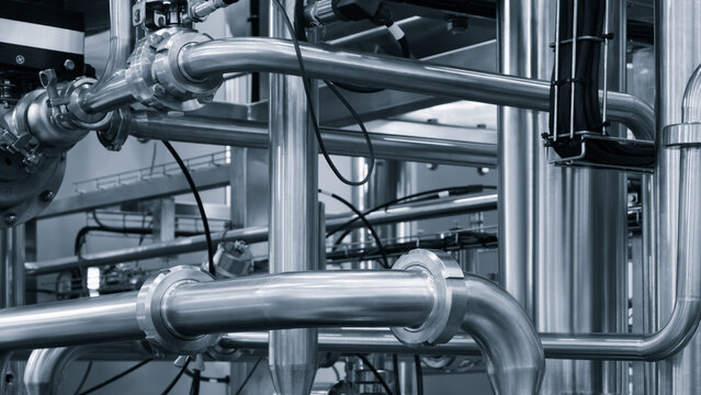 Industrial piping system in monochrome. Stainless steel pipes form complex network. Visible valves and connections in factory setting. Clean technical photography