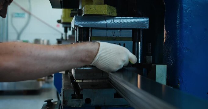 Punch press operator feeding metal sheet into stamping machine in industrial workshop, metal processing operation