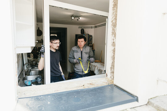 Two handsome workers measure and discuss the error in the dimensions of a window frame.