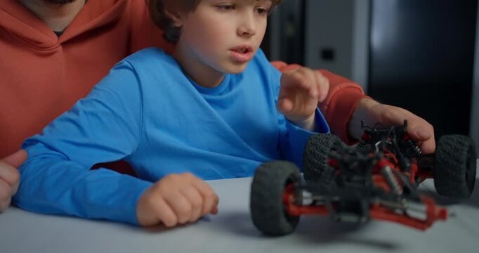 Father and young son examining a remote control car chassis at a table, learning mechanics together during a focused indoor family activity