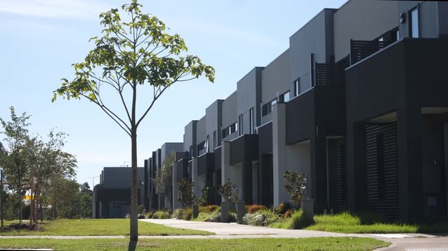 Townhouse development in suburban Melbourne, Australia, featuring contemporary multi-story residential architecture, landscaped nature strip,young trees, and pedestrian pathways in a new estate.