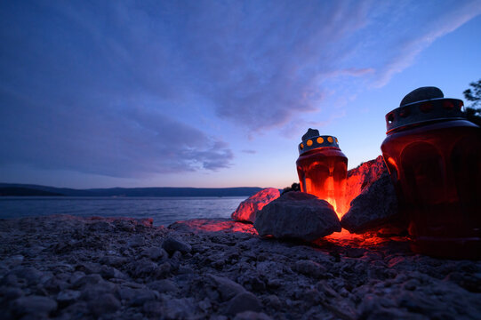 Two glowing red memorial lanterns burn on pebble beach at twilight by the sea