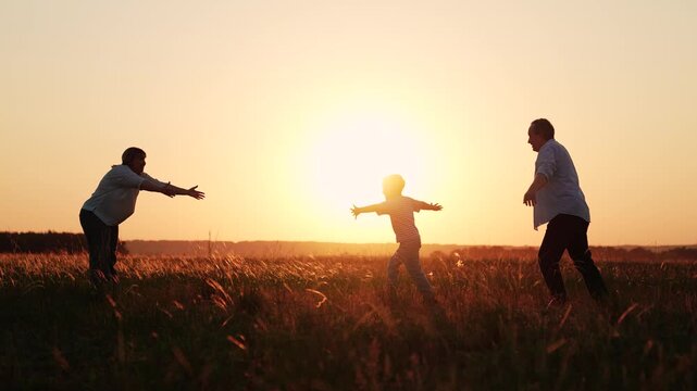 Child boy runs from dad to mom, hugging parents. Family picnic in field, sunset. Child playing outdoors with mother father. Family, mom dad, kid son love mother father. People in park. Silhouettes