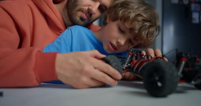 Father and young son carefully repairing a remote control car together at a table, sharing focused hands-on learning and family bonding indoors