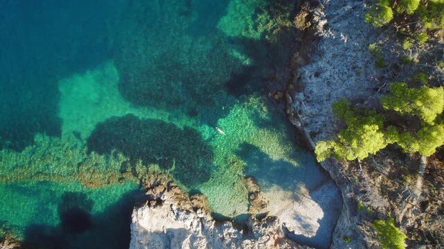 Woman floats in calm cove surrounded by rocky cliffs and clear green blue water