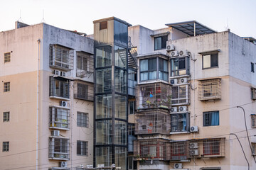 Older walk-up apartment building in Liuzhou, China, retrofitted with an external glass elevator to improve accessibility for residents in aging mid-rise housing block in residential neighborhood © Doublelee