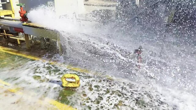 water from ship fire line sprayed on deck with big pressure, make foam, drops and spread on deck