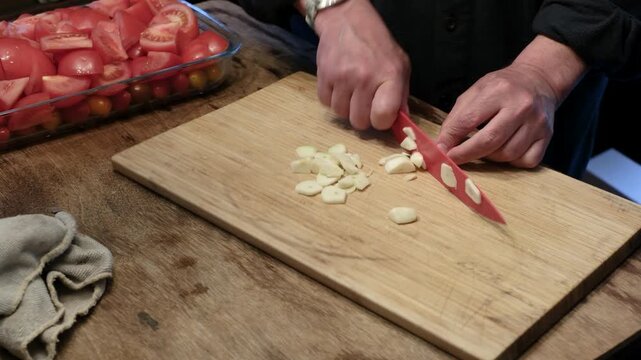 Chef slicing garlic on wooden cutting board.