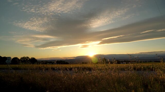 Atardecer en una carretera secundaria con luz c&aacute;lida de fondo y siluetas de coches pasando a contraluz.