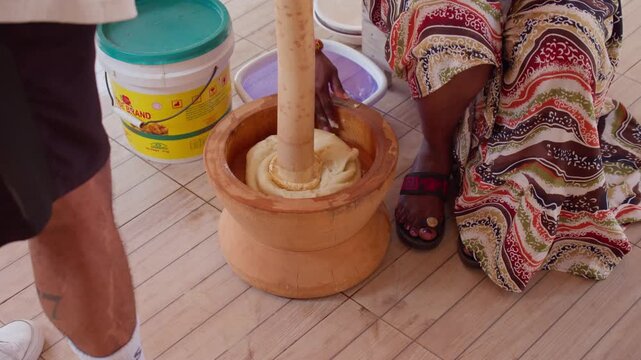 Ghanaian woman preparing traditional fufu using wooden pestle and mortar, pounding cassava dough in Accra, Ghana for cultural meal, african heritage and cuisine