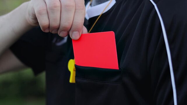 Soccer referee taking a red card from pocket during a football match. Close-up