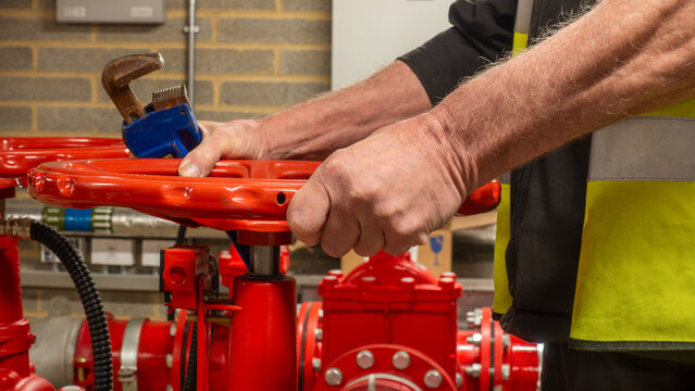 Sprinkler system service engineer operating a red flow valve with a wrench in his hand. Wet fire safety sprinkler system being maintained by a specialist
