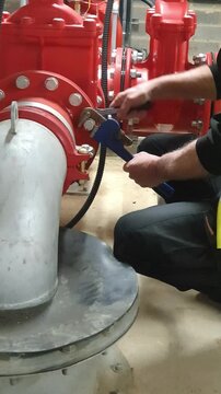 Fire system and specialist sprinkler engineer using wrench and ratchet to tighten a red pipe flange. Residential building fire and safety planned maintenance