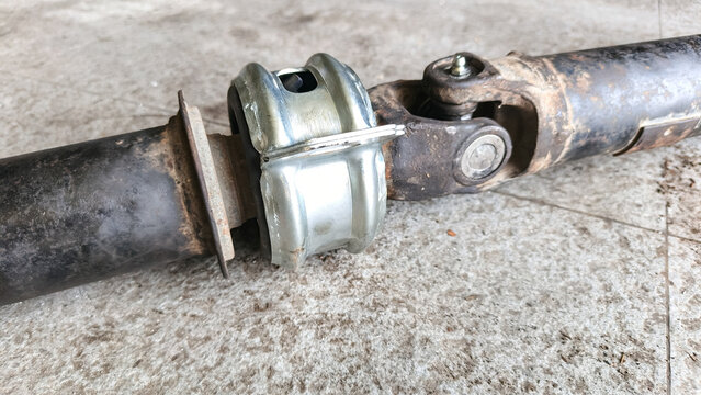 Car driveshaft with a new center support bearing and universal joint on a concrete floor. Automotive repair and mechanical maintenance concept.
