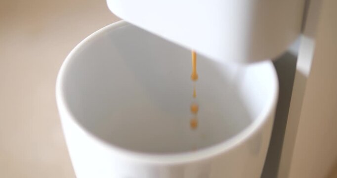 Cinematic shallow focus of fresh espresso coffee dripping from machine into a white ceramic cup, slow living morning routine concept