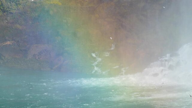 Rainbow arching through mist and spray over a powerful waterfall surrounded by rocky cliffs in autumn in 120fps 4K Slow Motion