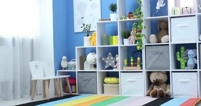 Shelving unit with different toys and decor near blue wall in child's room. Camera moving left