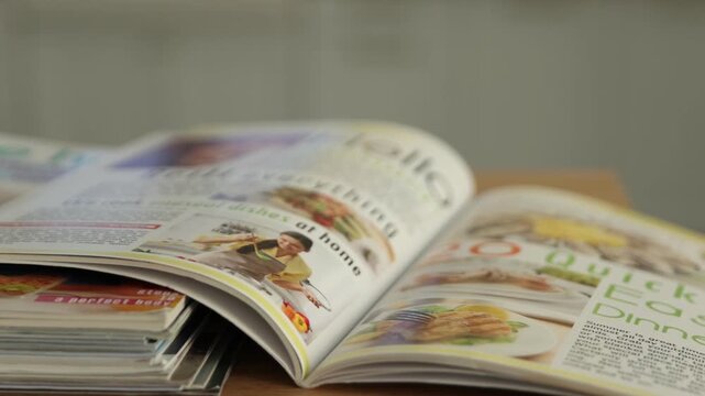 Many lifestyle magazines on wooden table indoors, closeup. Camera moving right