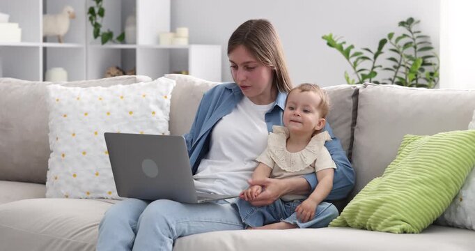 Young mother with her baby working on sofa at home