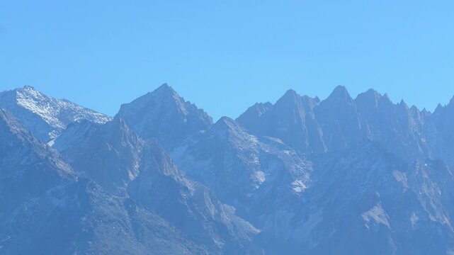 Mountain peaks with light snow dusting standing majestically against a clear blue sky during a bright sunny day in 120fps 4K Slow Motion