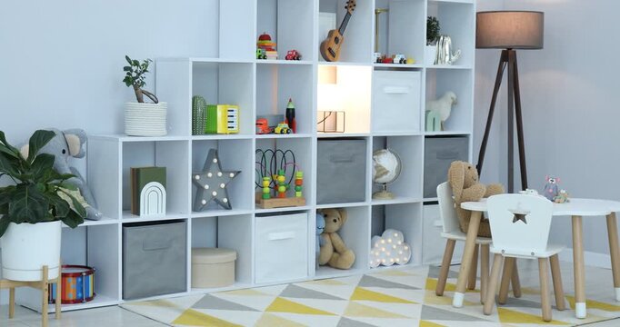 Shelving unit with different toys and decor near light grey wall in child's room. Camera moving left