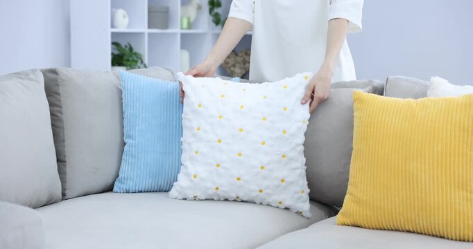Woman putting soft colorful pillow onto gray sofa indoors, closeup