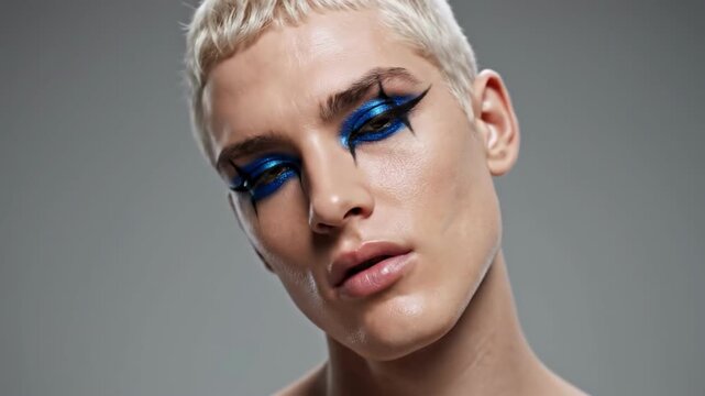 Portrait of a person with short blonde hair and striking blue eyeliner, exuding a sense of boldness and confidence.