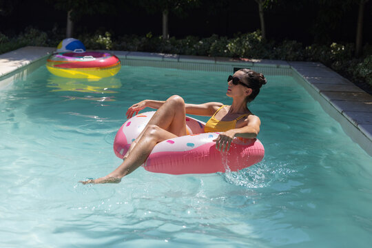 Pink donut inflatable with sprinkles is floating in rectangular pool under bright sunlight