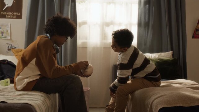 Medium full side shot of two thrifty teenage young black brothers opening piggy bank, counting money, checking watermarks on dollar bills while saving for new toys. Family economy, financial planning