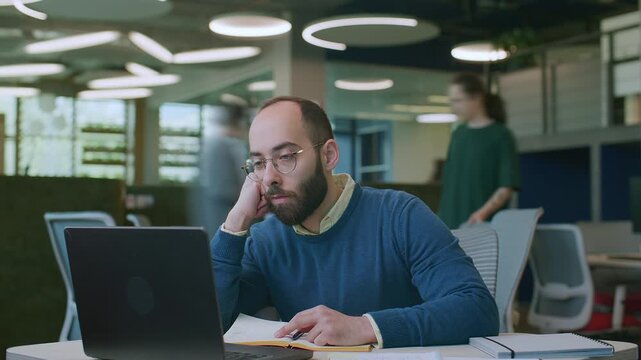 Time lapse of exhausted business manager with glasses and beard leaning his head on hand and staring at laptop screen in boredom. Zoom out shot