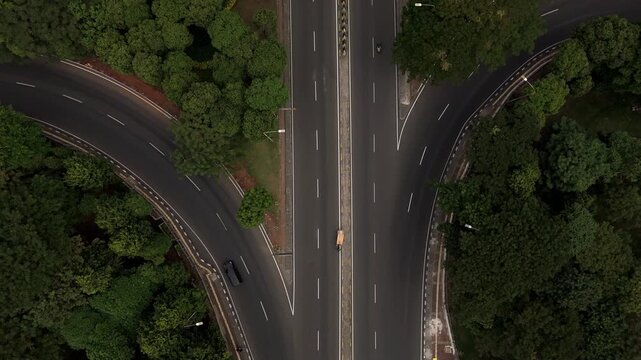 Color graded top down aerial view of a multi lane highway highway splitting into different directions surrounded by lush green trees