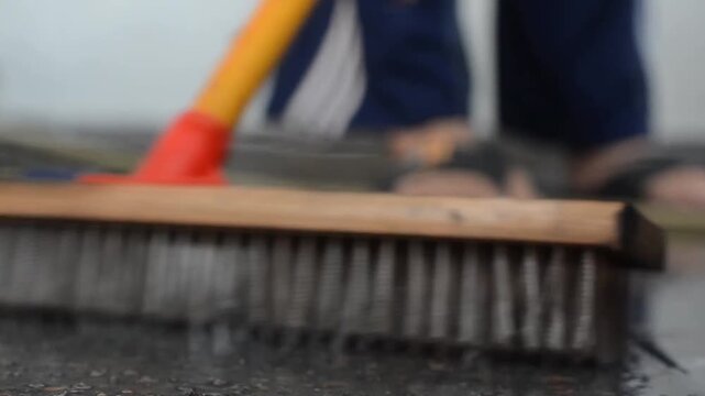 Low angle close up of a wooden brush scrubbing a wet floor outdoors during a house chore or cleaning activity