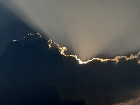 Stunning dramatic sky showcasing a majestic silver lining effect. Powerful golden and white sun rays burst from behind a dark, heavy storm cloud, creating a brilliant rim light contrast.