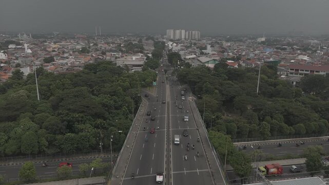 Top down aerial view of highway split with vehicles driving through lush green trees on asphalt road