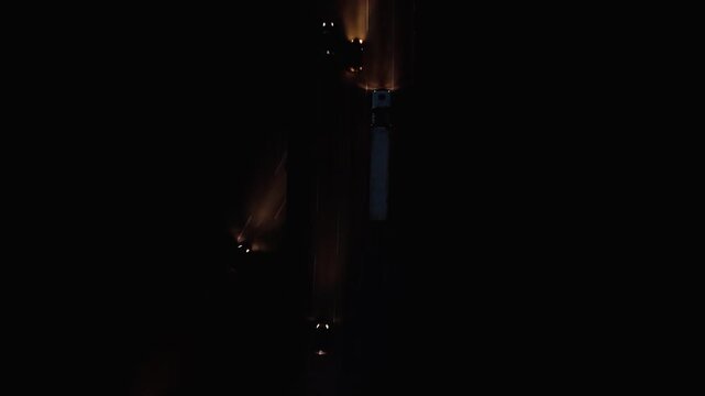 Night aerial view from overhead of Rodovia dos Imigrantes highway with vehicle lights, tilting up to mountain silhouette and twilight sky at Santos, Brazil. Overhead and tracking and cam movement