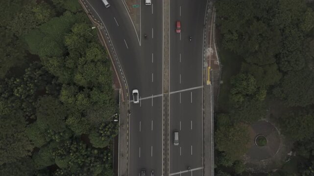 Top down aerial view of highway intersection with moving cars and green trees in city