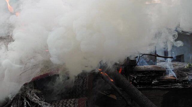 Slow motion 4K footage of burning trash and an old carpet producing thick smoke near houses.