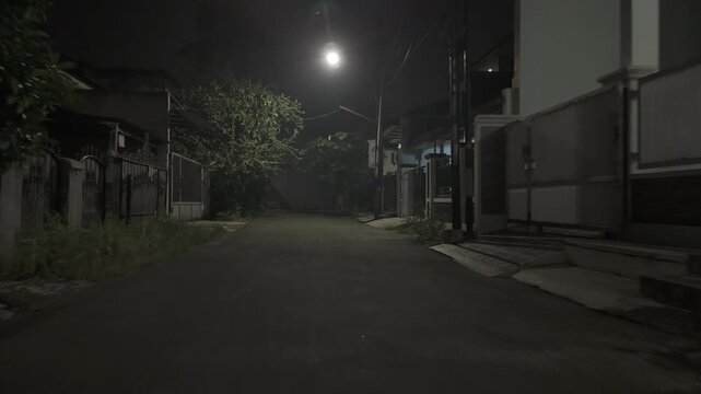Quiet empty suburban street at night under a single bright streetlight with puddles after rain