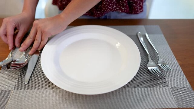 Hands Arranging Silverware and White Ceramic Plate on Wooden Dining Table