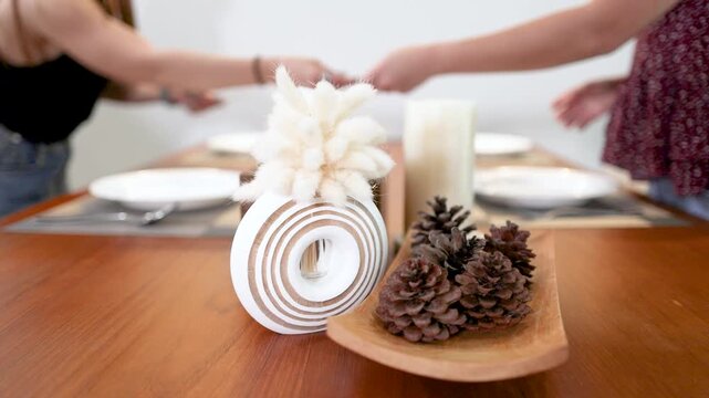 Two Women Setting a Minimalist Dining Table with Pine Cone Centerpiece