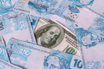 Fototapeta premium One hundred American dollar bill, stuck between 100 Brazilian real bills. Economic crisis and drop in the American currency