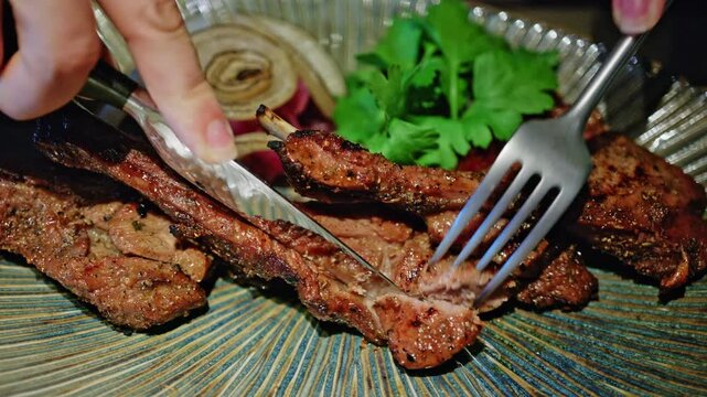 Close up shot of grilled pork ribs glazed with a savory marinade, being cut with a knife and fork on a ceramic plate
