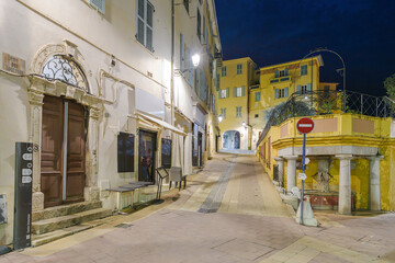 Fototapeta premium Night view on Rue des Logettes looking towards one of the tunneled entrances into the medieval old town district of Vieux-Menton, in Menton, France, on the French Riviera.
