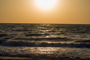 Obraz premium Beautiful golden sunset over the ocean with gentle waves rolling onto the shore and sunlight reflecting across the water surface.