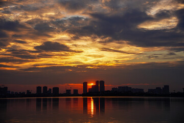 Fototapeta premium Sunset Silhouette over the City: The silhouette of a cityscape against the backdrop of a radiant sunset, with the sky ablaze with vibrant hues and reflections dancing on the water, creates a stunning.